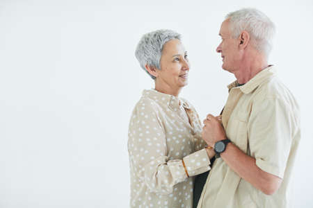 Happy elderly couple looking at each other with love and dancing against the white background