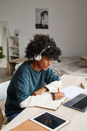 Vertical portrait of African-American teenage boy studying at home or in college dorm and using laptopの写真素材