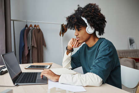 Side view portrait of male African-American teenager studying at home and using laptopの写真素材