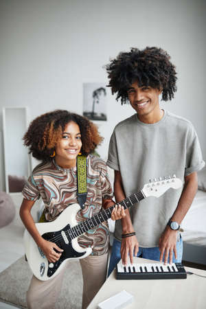 Vertical portrait of two African-American young people playing music at home and smiling at camera, brother and sisterの写真素材