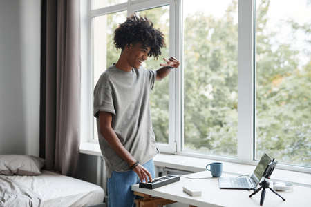 Portrait of young African-American man playing music at home and recording video or livestream, copy...
