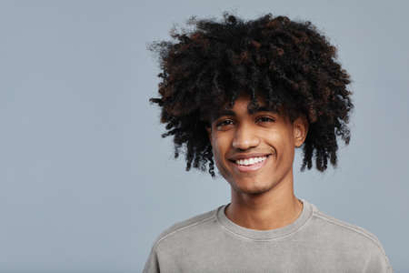 Minimal portrait of young African-American man with natural curly hair smiling at camera while posing against blue background in studio, copy spaceの写真素材