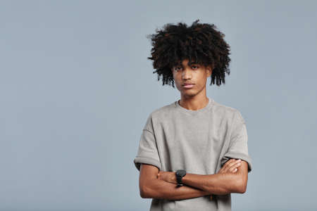 Minimal waist up portrait of young African-American man with natural curly hair looking at camera while standing against blue background in studio, copy spaceの写真素材
