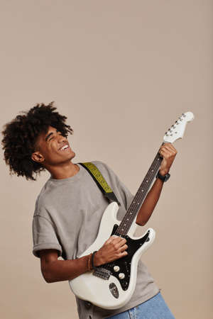 Minimal vertical portrait of young African-American man playing electric guitar against neutral beige background, copy spaceの写真素材