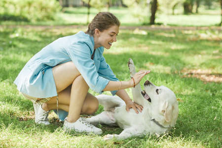 Full length portrait of smiling young woman playing with dog outdoors while enjoying walk together...