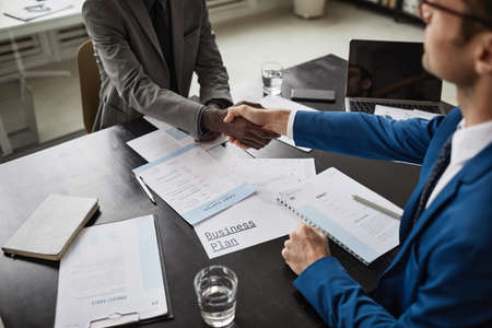 Close up of two businessmen shaking hands over table during meeting in office, copy space