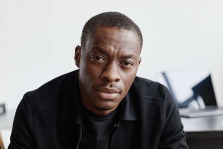 Close up portrait of serious African-American man in black looking at camera in minimal interiorの写真素材