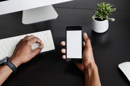 Minimal close up of male hands holding smartphone with blank screen while working at black desk,...