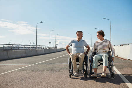 Full length front view portrait of adult couple in wheelchairs chatting outdoors and enjoying city life, copy spaceの写真素材