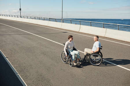 High angle portrait of adult couple in wheelchairs chatting outdoors and enjoying city life, copy spaceの写真素材