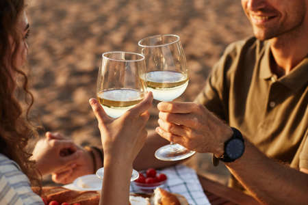 Close up of young couple drinking wine outdoors on beach while enjoying romantic date at sunset, copy spaceの写真素材
