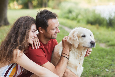 Side view portrait of happy young couple with dog sitting on green grass outdoorsの写真素材