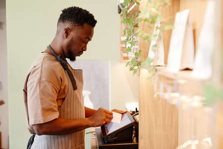 Horizontal side view shot of modern small cafe worker working with customer taking order using cash...