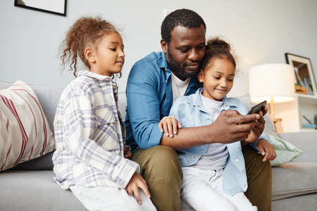 Portrait of smiling African-American father using smartphone with two little girls, copy spaceの写真素材