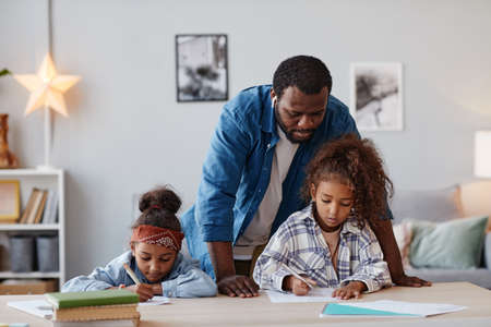 Portrait of African-American father doing homework with two little girls at home, copy space