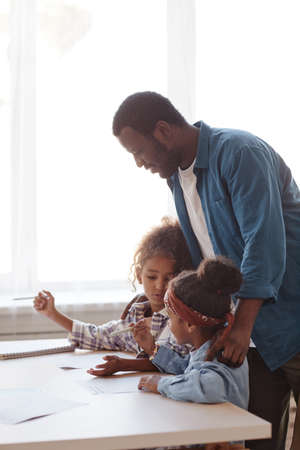 Vertical side view portrait of caring African-American father doing homework with two little girls at homeの写真素材