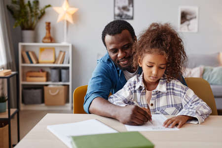 Portrait of caring African-American father doing homework with daughter at home, copy spaceの写真素材