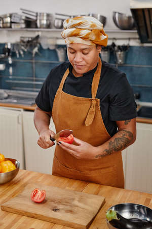 Vertical portrait of tattooed woman cooking vegetables in kitchen interior