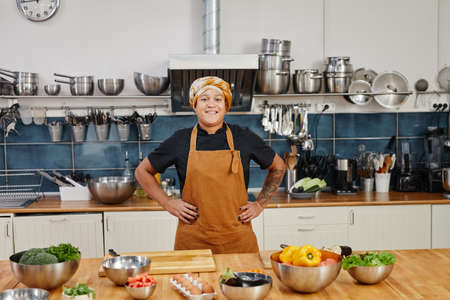 Portrait of smiling female cook looking at camera while posing in industrial kitchen interior, copy...
