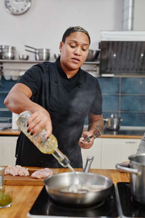 Vertical portrait of tattooed female chef frying meat while cooking in professional kitchen