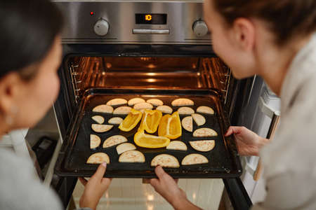 High angle close up of two young women opening oven in professional kitchen, copy spaceの写真素材