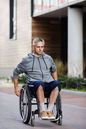 Senior man with disability riding in wheelchair along the street in the cityの写真素材
