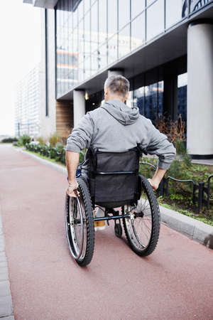 Rear view of mature male patient riding in wheelchair along the street outdoorsの写真素材