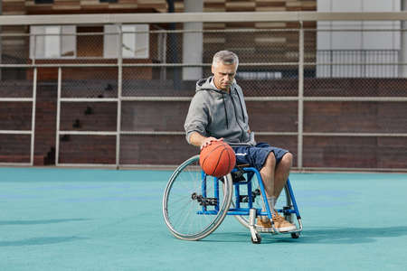 Mature man in wheelchair playing basketball on the sport ground outdoors