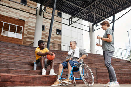 Paraplegic man talking to the athlete after basketball game while they sitting on the stadiumの写真素材