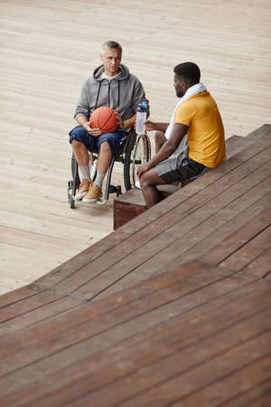 African young man talking to mature man with disability while sitting outdoorsの写真素材