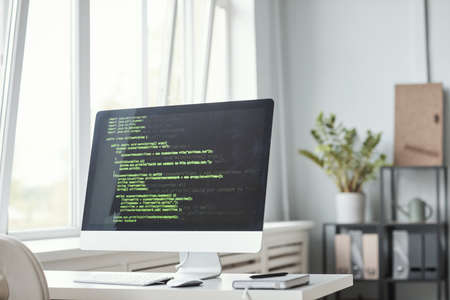 Background image of PC screen with green code lines on desk in software development office interior,...