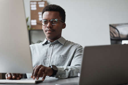 Front view portrait of young African-American man using computer and writing code in software...