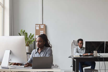 Wide angle portrait of two African-American young people using computers while working in software development office, copy spaceの写真素材