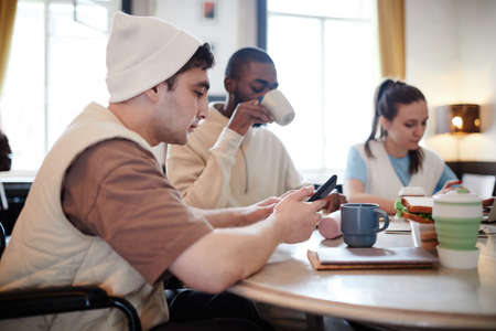 Boy using mobile phone while sitting at the table together with his friends after schoolの写真素材