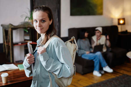 Portrait of college student with backpack behind her back holding books and looking at camera, she finishing her lessonsの写真素材