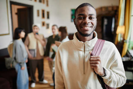 Portrait of African happy man with backpack behind his back smiling at camera while standing at universityの写真素材