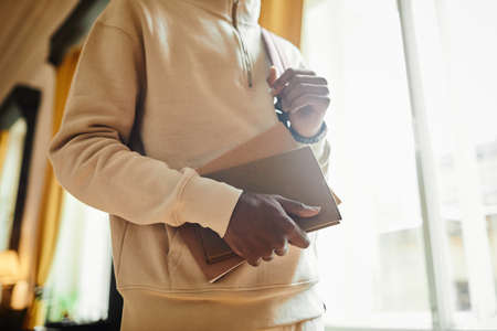 Close-up of African student with backpack behind his back holding book studying at universityの写真素材