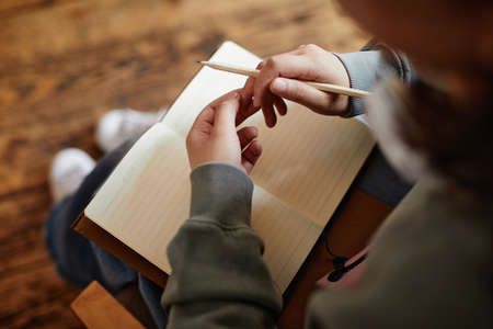 Close-up of woman sitting with notebook on her knees and writing her plans in it or doing homeworkの写真素材