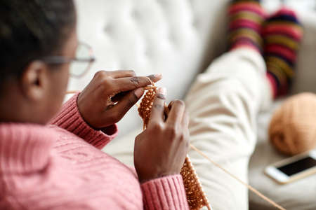 Close up of young African-American woman knitting at home while enjoying cozy weekend, copy space