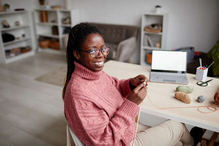 Portrait of young African-American woman knitting at home and smiling at camera, copy spaceの写真素材