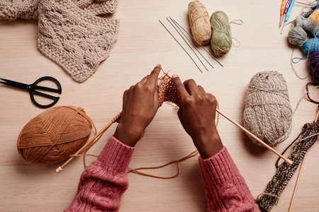 Top view of female hands knitting against wooden table in cozy light, copy spaceの写真素材