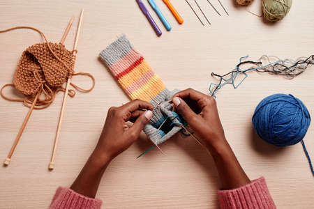 Top view close up of female hands knitting against wooden table in cozy light, copy spaceの写真素材