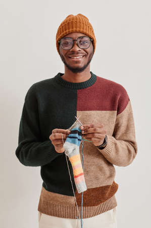 Minimal vertical portrait of young African-American man knitting and smiling at cameraの写真素材