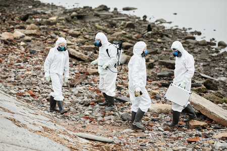 Group of workers wearing hazmat suits walking by water outdoors, toxic waste conceptの写真素材