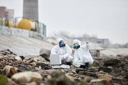 Full length portrait of two workers wearing hazmat suits collecting probe samples in industrial area, toxic waste conceptの写真素材