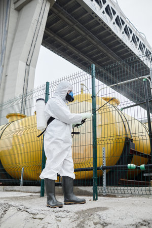 Full length portrait of worker wearing protective suit disinfecting industrial areaの写真素材