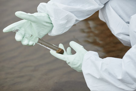 Close up of unrecognizable scientist wearing hazmat suit collecting water probes, focus on gloved hands holding test tubeの写真素材