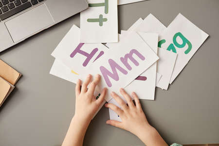 Close-up of little girl sitting at the table and learning cards with English letters during a lessonの写真素材