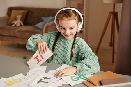 Little girl sitting at the table and learning English by audio using wireless headphonesの写真素材