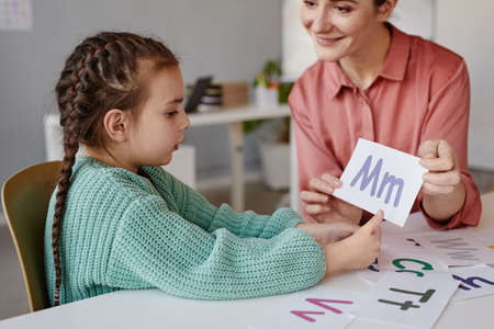 Little girl learning the English alphabet together with the tutor at the tableの写真素材